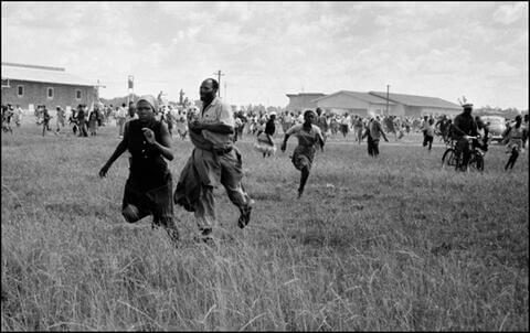 The police open fire and the crowd flees. Police can be seen in the background standing on their armored cars continuing to fire into the crowd as they run. Monday, March 21, 1960.